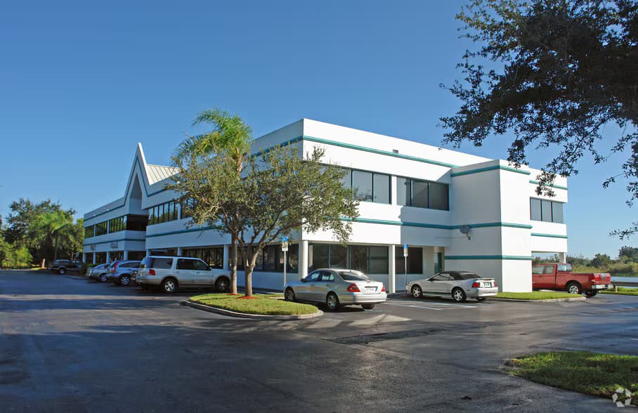 Two-story white office building with teal trim and cars parked in a paved lot.