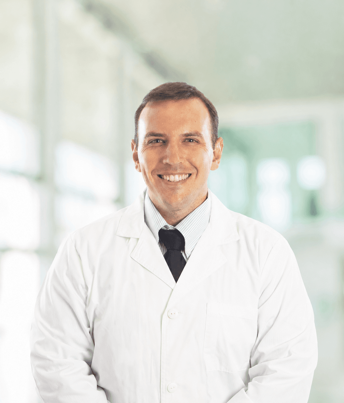 Professional male doctor smiling while wearing a white lab coat and dark necktie.